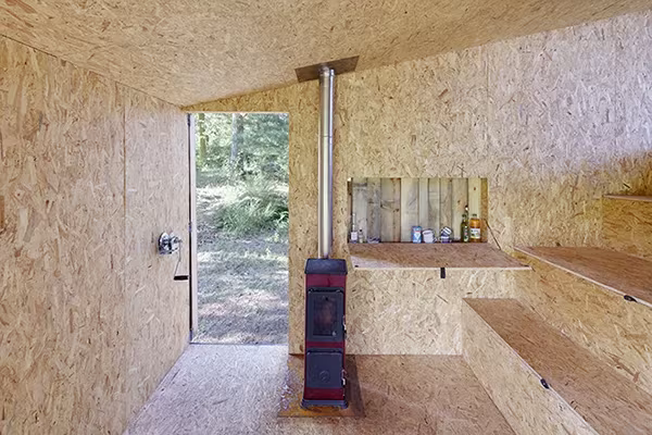 Cabaña en Bohemia por dentro: paredes de OSB, estufa de leña, baldas y puerta abierta al bosque