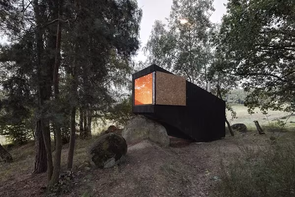 Cabaña de madera negra de Uhlik Architekti sobre una roca en un claro del bosque de Bohemia