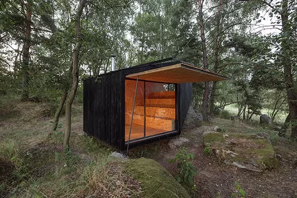 Cabaña en Bohemia con la fachada abierta y el interior de madera iluminado entre los árboles