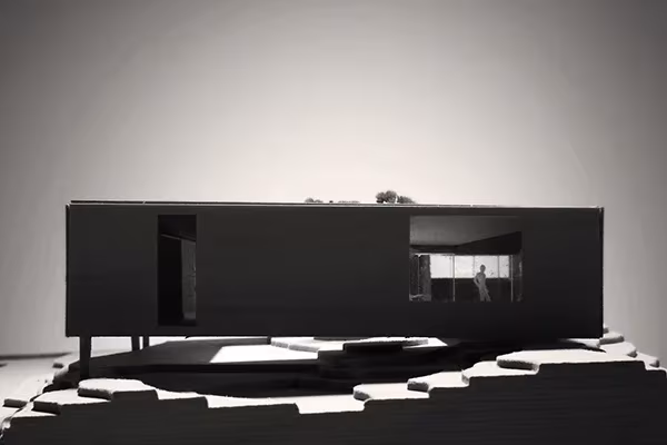 Maqueta alargada y oscura de la Casa Cubo en Veierland, elevada sobre pilares encima de un terreno escalonado