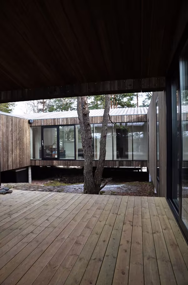 Porche cubierto de la Casa Cubo en Veierland con suelo de tarima que se abre al patio con un árbol