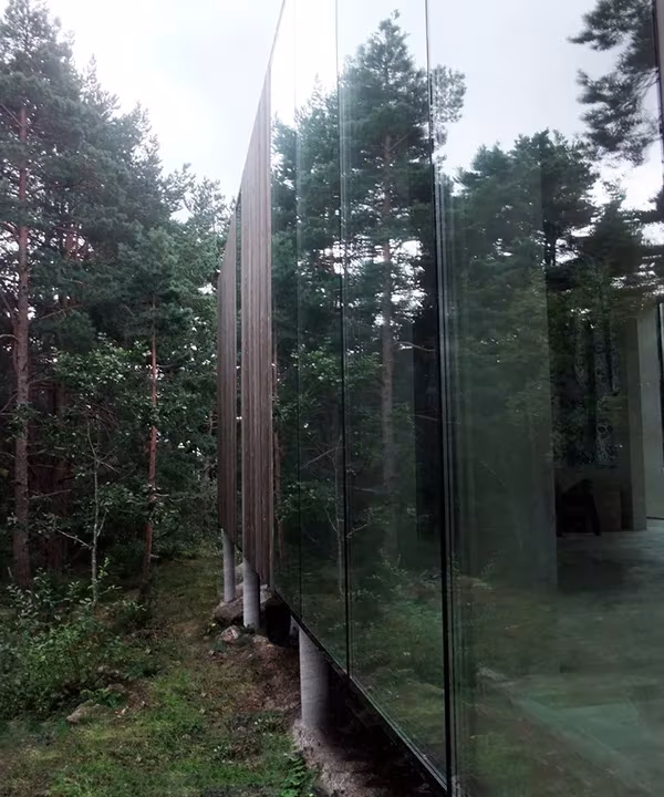 Gran paño de vidrio de la Casa Cubo en Veierland que refleja el pinar que la rodea