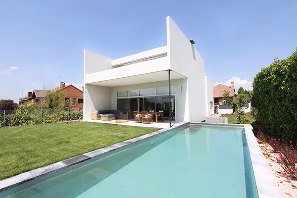 Casa Eficiente blanca de ÁBATON con porche, césped y piscina alargada en primer plano
