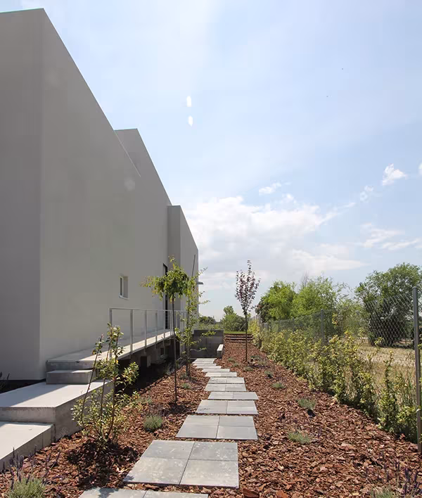 Fachada lateral gris de una Casa Eficiente de ÁBATON con camino de losas y jardín de corteza