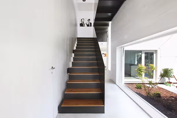 Escalera de chapa negra con peldaños de madera en el interior blanco de una Casa Eficiente de ÁBATON