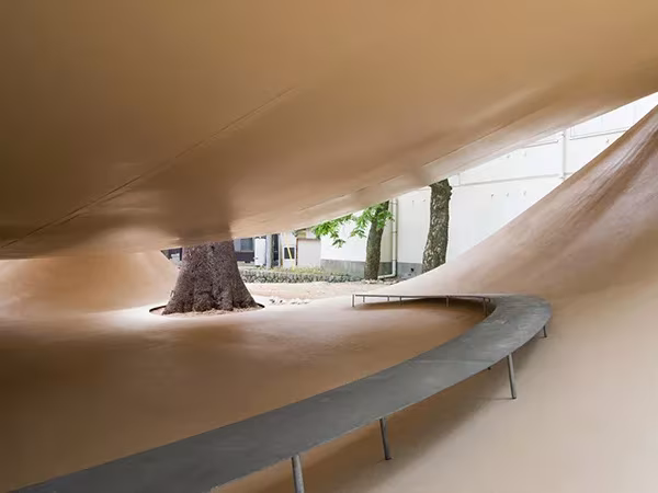 Interior curvo del Fukita Pavilion de Ryue Nishizawa con un banco metálico sinuoso y un árbol al fondo