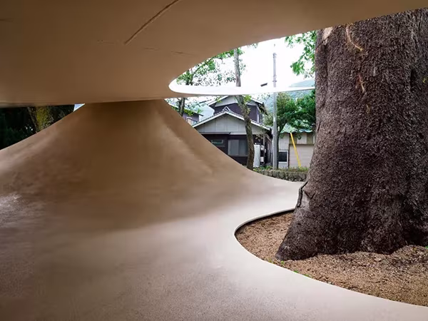 Grueso tronco que atraviesa la cubierta curva del Fukita Pavilion, con casas japonesas al fondo