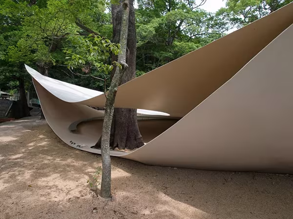 Láminas metálicas curvadas del Fukita Pavilion de Ryue Nishizawa abrazando un árbol en un patio de tierra