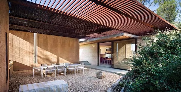 Patio de grava de la NAPA House de Steven Harris con mesa larga bajo una pérgola de lamas de acero