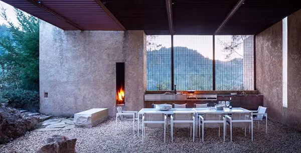 Comedor exterior de la NAPA House con chimenea en muro de tierra y vistas a las colinas del valle