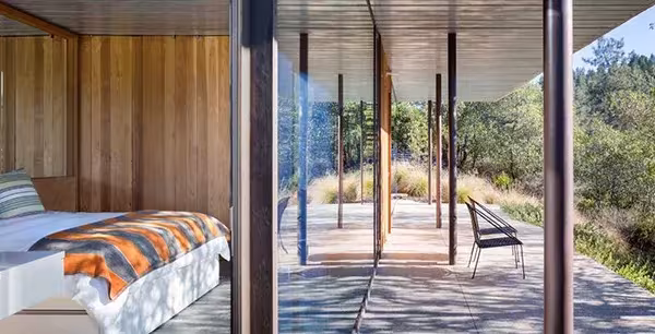 Dormitorio con paredes de madera de la NAPA House que se abre a un porche cubierto con pilares de acero