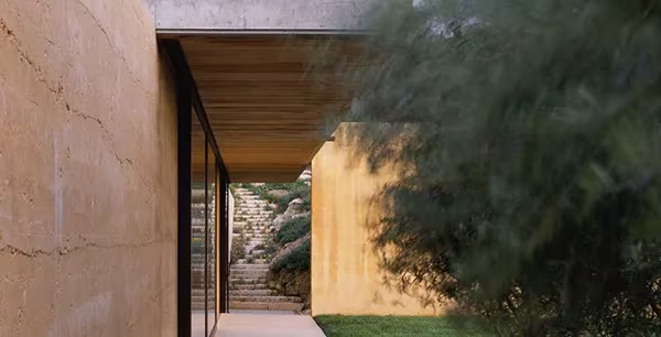 Muro de tierra apisonada y paso cubierto de la NAPA House que enmarca una escalera exterior de piedra