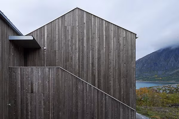 Vega Cottage de Kolman Boye Architects, volumen de madera oscura ante el fiordo y las montañas noruegas