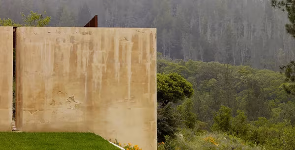 Muro macizo de tierra apisonada de la NAPA House sobre el césped, frente a las colinas boscosas del valle
