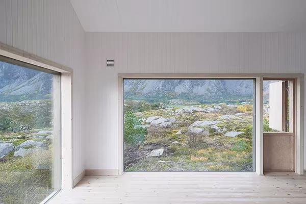 Interior blanco de la Vega Cottage de Kolman Boye Architects con grandes ventanales abiertos al paisaje rocoso noruego