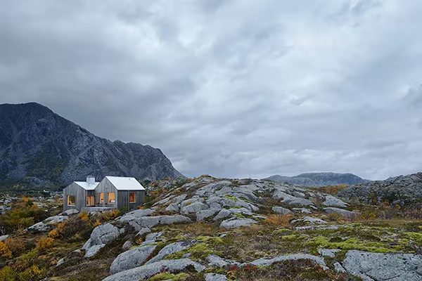 Vega Cottage de Kolman Boye Architects sobre lomas de granito y musgo bajo un cielo nublado, con montañas detrás