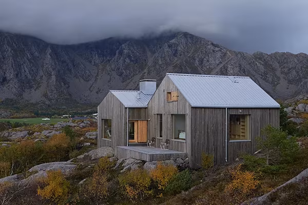 Vega Cottage de Kolman Boye, dos volúmenes de madera a dos aguas sobre granito bajo montañas con niebla