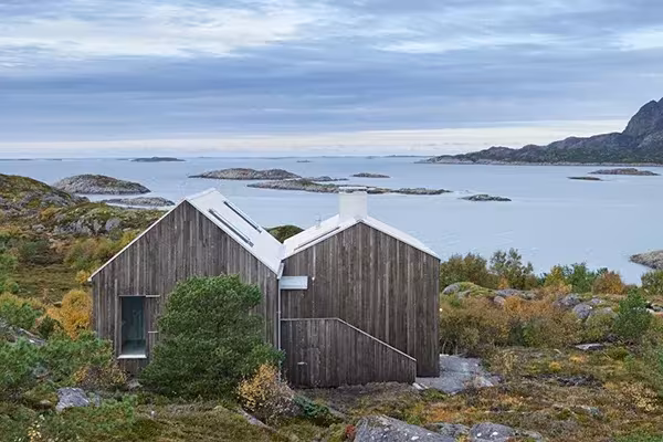 Vega Cottage con fachadas de madera gris sobre la costa rocosa, frente a islotes del Mar de Noruega