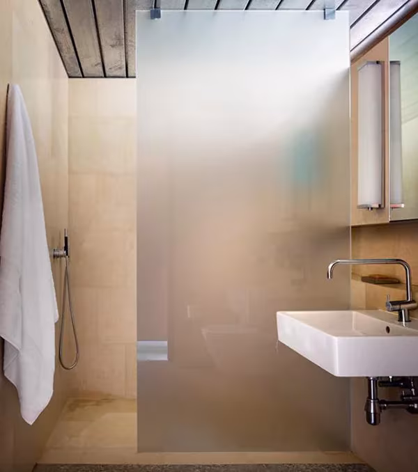 Baño de la NAPA House con lavabo blanco suspendido, ducha tras vidrio esmerilado y toalla colgada