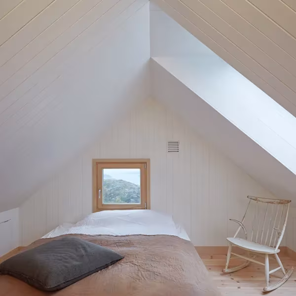 Dormitorio abuhardillado de la Vega Cottage con cama, mecedora de madera y pequeña ventana al paisaje