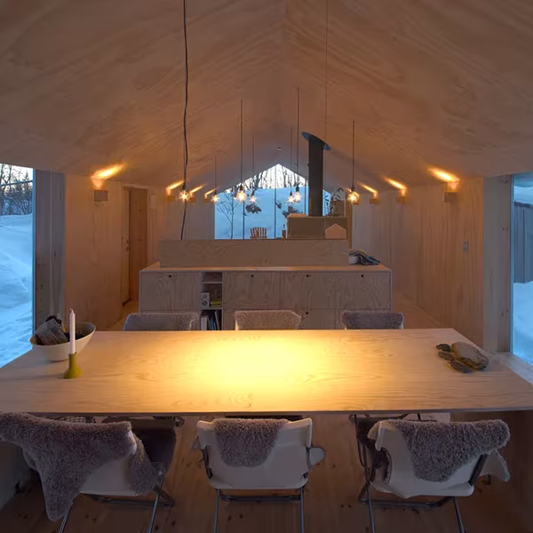Comedor de V-Lodge con luz cálida, sillas cubiertas de piel de oveja y techo inclinado de contrachapado