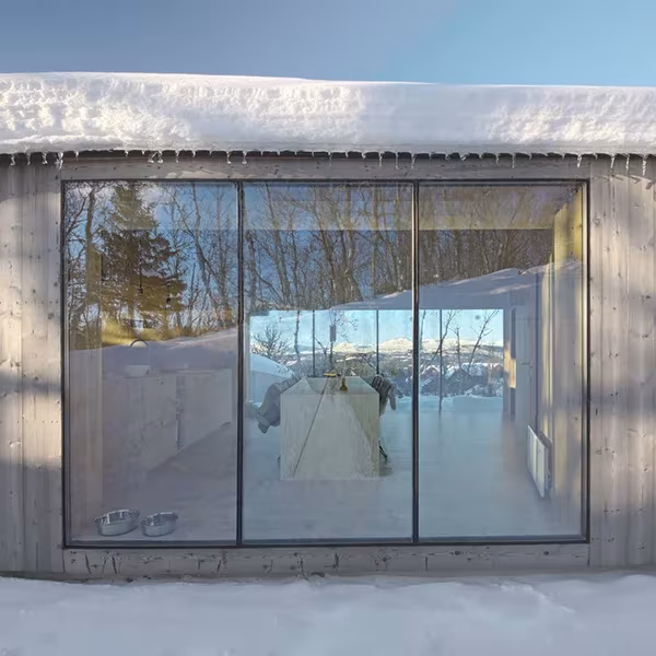 Fachada acristalada de V-Lodge de Reiulf Ramstad con la cubierta cargada de nieve y el interior visible