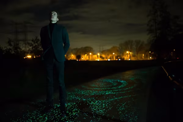 Hombre de pie de noche sobre el carril bici Van Gogh de Daan Roosegaarde, con piedras luminosas en espiral