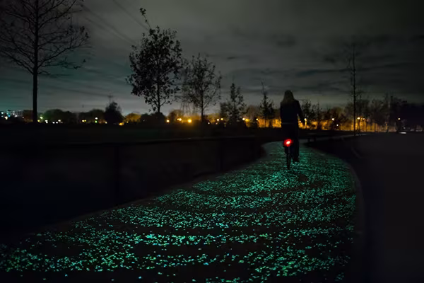 Ciclista con luz trasera roja recorriendo de noche el carril bici luminoso Van Gogh entre árboles