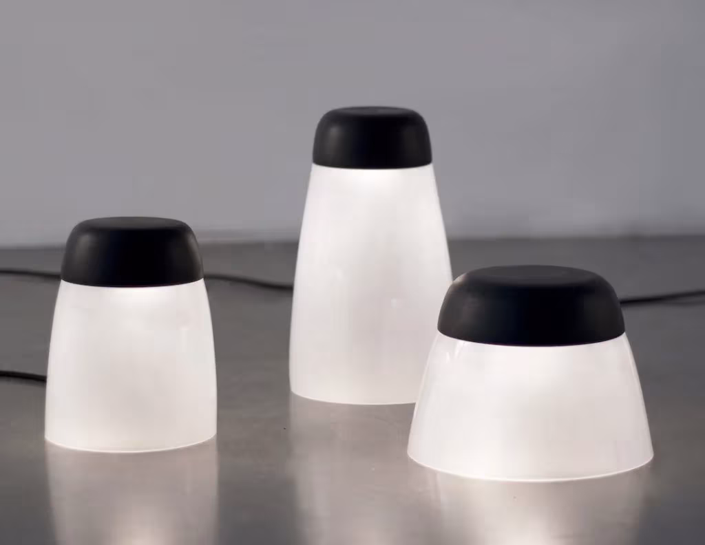 Tres lámparas de vidrio esmerilado con tapa negra encendidas sobre una superficie gris