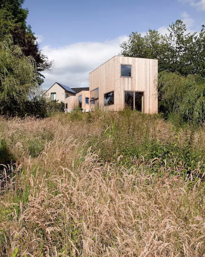 Casa de las 14 fachadas, volúmenes cúbicos de madera clara tras un prado de hierba alta en Bélgica