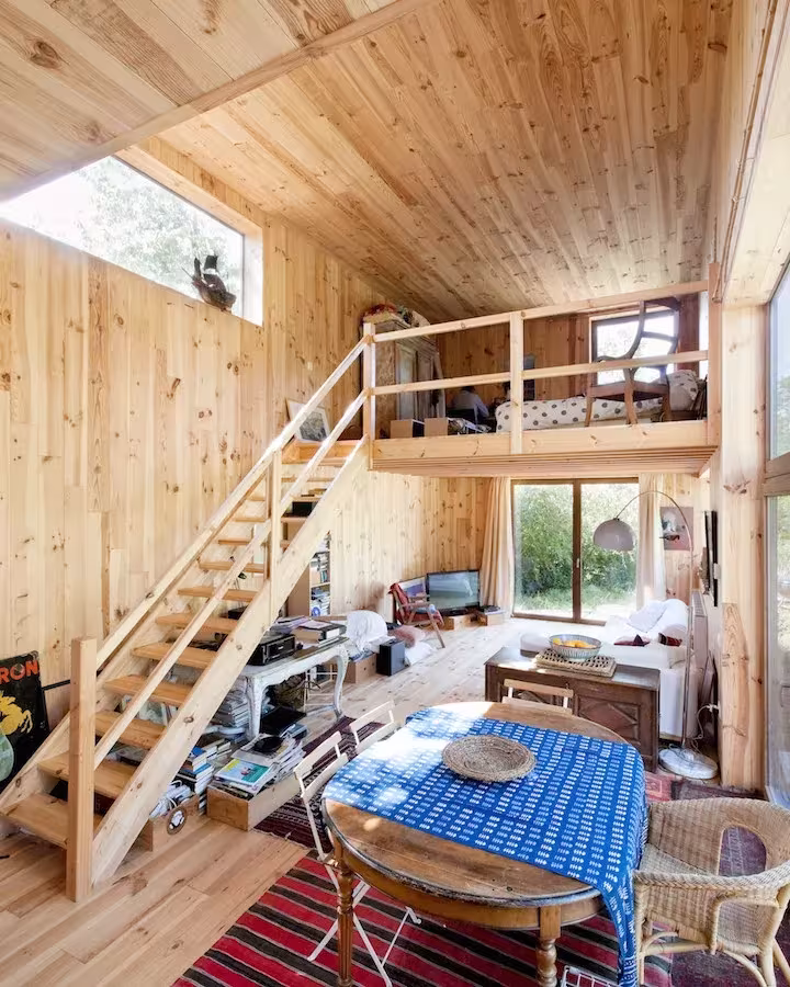 Interior de pino de la Casa de las 14 fachadas con escalera a un altillo y mesa con mantel azul