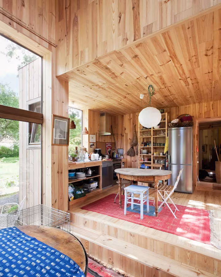 Cocina con estanterías abiertas y mesa redonda en la Casa de las 14 fachadas, forrada de madera de pino