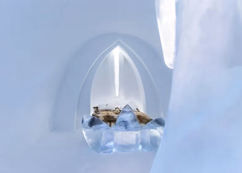 Suite del Icehotel con arco apuntado de hielo iluminado y cama con pieles sobre una base cristalina