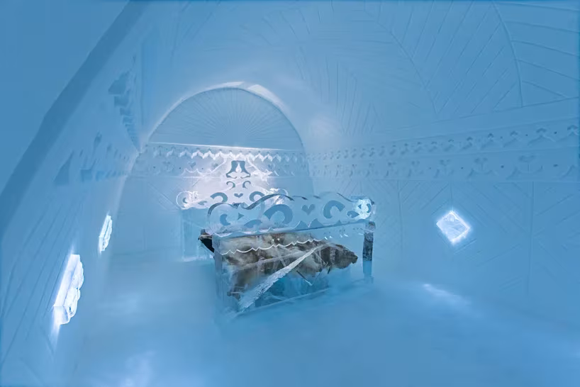 Suite azulada del Icehotel con bóveda decorada y cama con cabecero de hielo calado y pieles