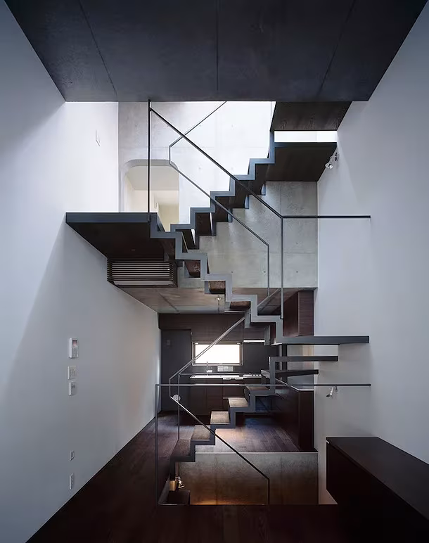 Escalera de peldaños volados oscuros en un espacio blanco de doble altura de la Casa Lattice en Tokio