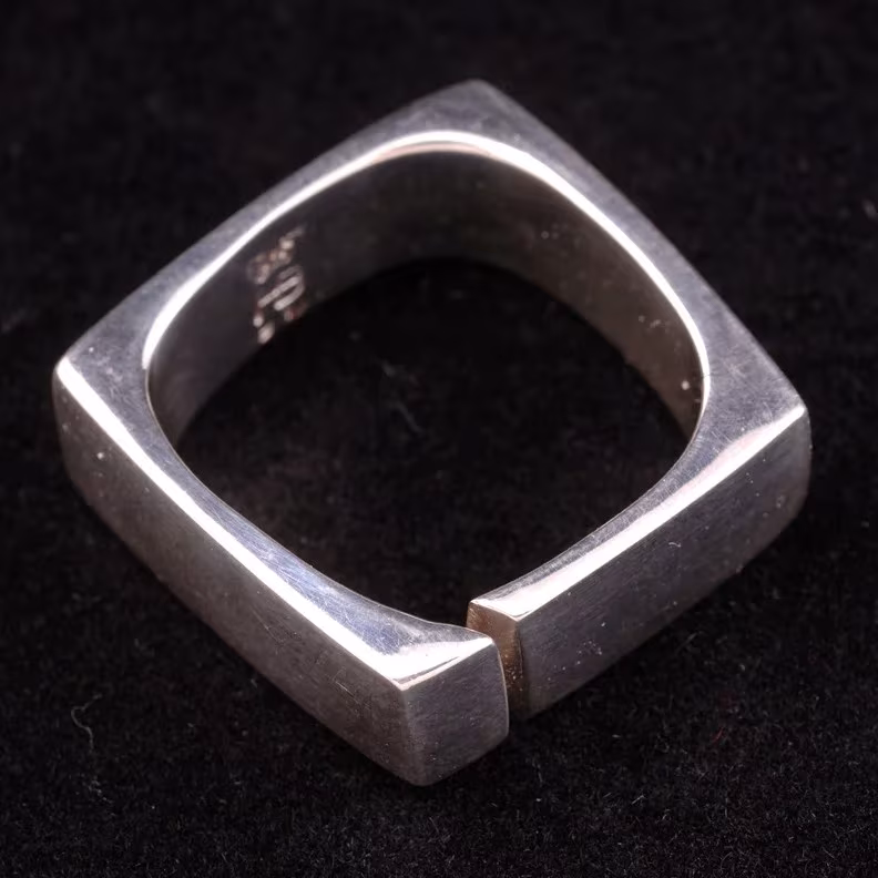 Anillo cuadrado de plata con bordes redondeados y abertura lateral de Harry Bertoia sobre fondo negro