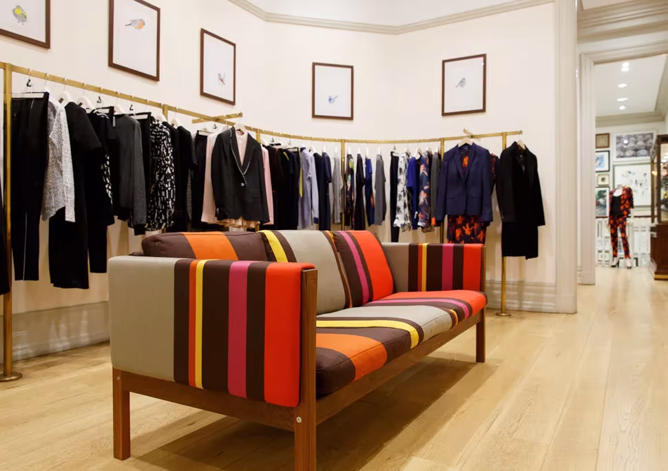 Sofá CH163 de Wegner tapizado con rayas de colores de Paul Smith en una tienda con ropa colgada