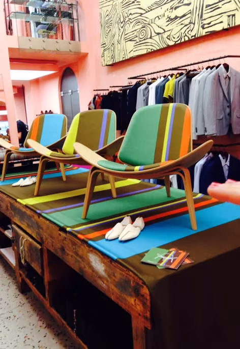 Sillas CH07 Shell tapizadas en colores vivos sobre una mesa a rayas en una tienda de Paul Smith