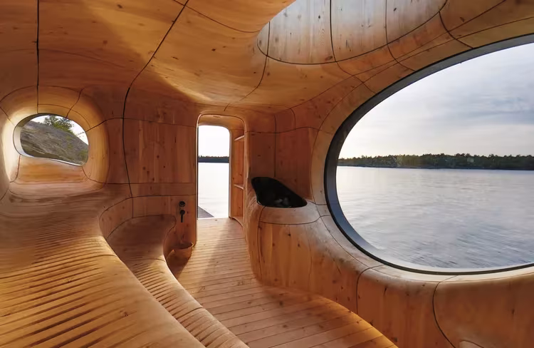Sala de la sauna Grotto con paredes ondulantes de cedro y gran ventana ovalada al agua