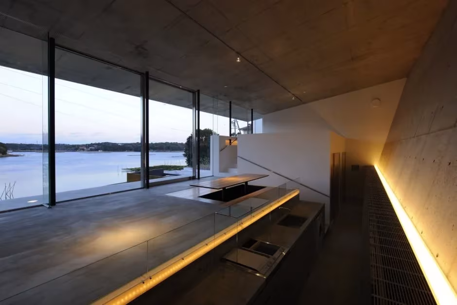 Cocina de la Beach House con encimera oscura iluminada por una línea de luz y ventanal hacia la bahía
