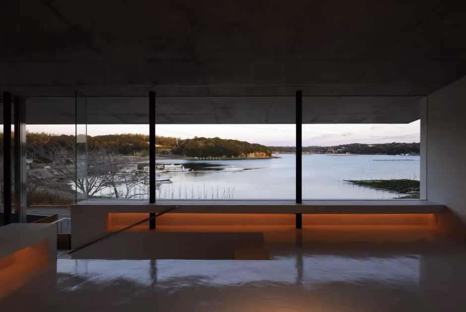 Salón de la Beach House en penumbra, con ventanal panorámico que encuadra la bahía y las islas al atardecer