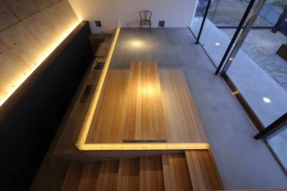 Vista cenital de la mesa de madera y el banco iluminado junto al ventanal en la Beach House de Shima