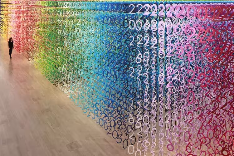 Bosque de números de papel de colores de Emmanuelle Moureaux suspendidos del techo, con una persona caminando