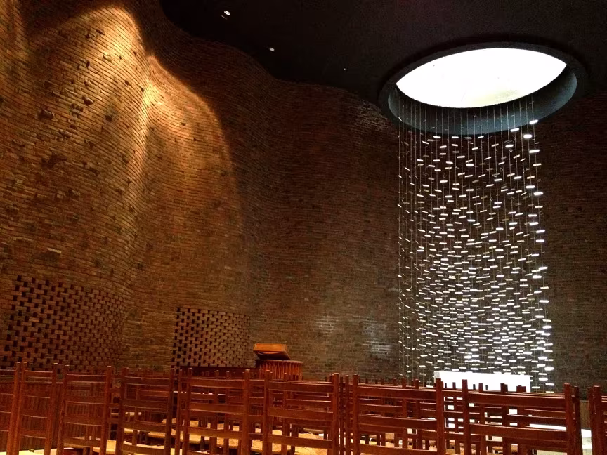 Capilla del MIT con muro de ladrillo ondulado y retablo de láminas metálicas de Harry Bertoia bajo un óculo