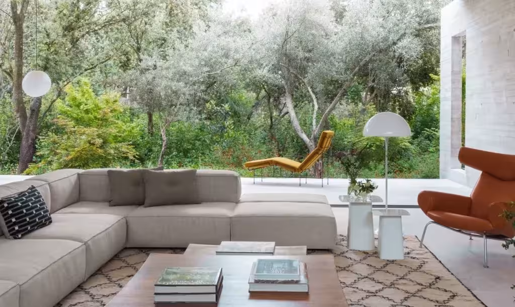Salón de ÁBATON con sofá modular claro abierto a un jardín de olivos y vegetación mediterránea