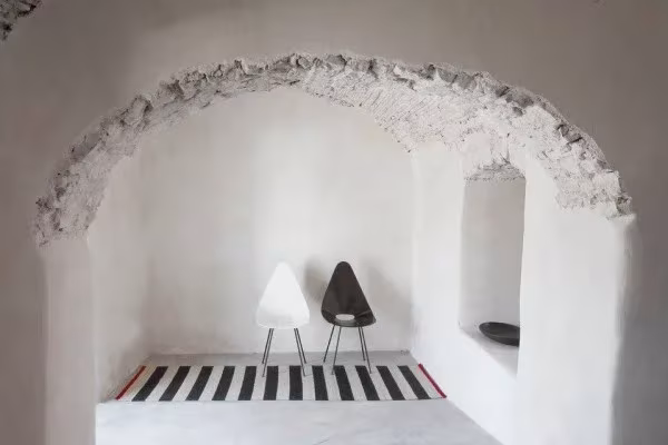 Alfombra Mélange a rayas blancas y negras de Sybilla bajo un arco de piedra encalado, con dos sillas