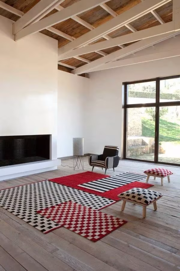 Salón con vigas de madera y alfombras Mélange de Nani Marquina en rojo, blanco y negro sobre tarima