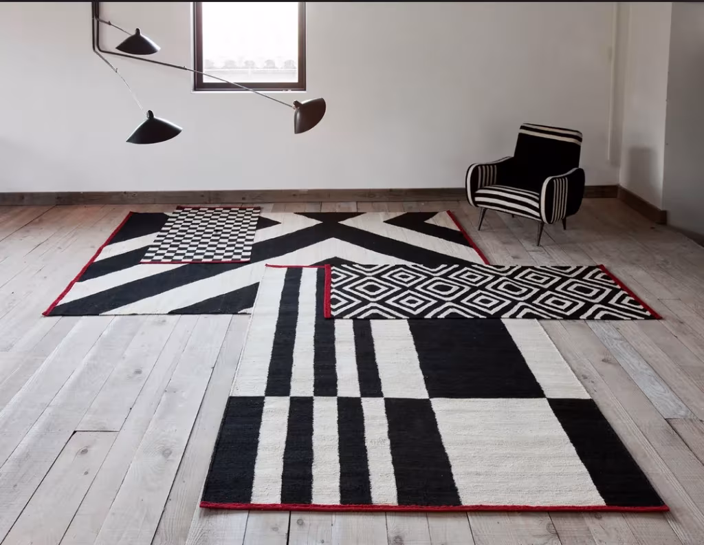 Alfombras geométricas Mélange superpuestas en blanco y negro, con butaca a rayas y lámpara de brazos