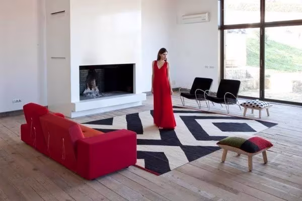 Salón con sofá rojo, chimenea blanca y alfombra Mélange en zigzag, con una persona de vestido rojo