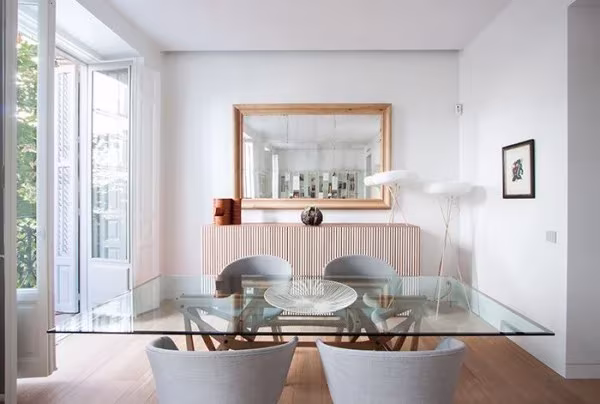 Comedor con mesa de cristal, sillas blancas tapizadas y espejo dorado, con lámpara Molo al fondo